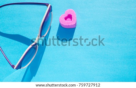Sunglasses and pirple candy in shape of heart on blue background.