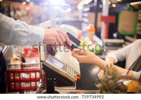 Side view close up of unrecognizable customer handing credit card to cashier paying via bank terminal at grocery store Royalty-Free Stock Photo #759734992