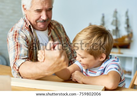 Portrait of white haired senior man armwrestling with  little grandson having fun together ant home