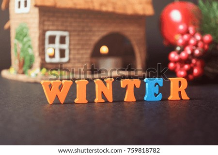 Winter is here. The floor is lined with colored letters on a black table on the background of the cones, a festive garland of Christmas trees and a clay house with a candle