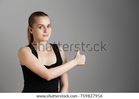 Portrait of young beautiful girl. Thumb up. Body language. Over grey background. Copy space.