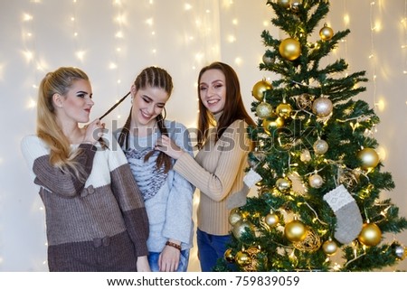 Girls friends decorating fur-tree near fireplace with candles and gifts. girls  dreaming. New year's eve. Christmas eve. Cozy holiday at the fur-tree with lights and gold decor.