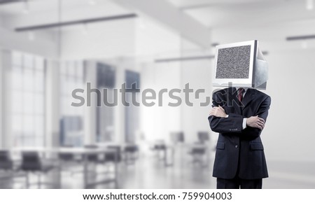 Cropped image of businessman in suit with monitor instead of head keeping arms crossed while standing inside office building.