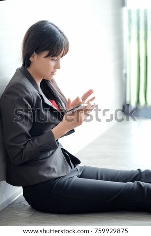 Beautiful asian businesswoman in suit jacket sitting on the floor of the conferrence room using smart phone seriously, technology concept. Cheerful girl playing game on smart phone in meeting room.