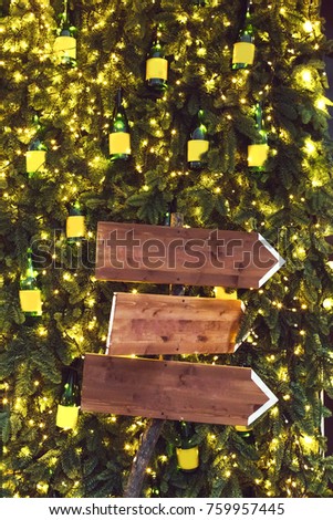 Three wooden pointer on background with fir branches in garlands. Christmas lights decoration, new year party