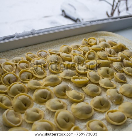 On the open window there are many homemade meat dumplings. Stocks for the winter, home food. It's snowing outside, cold winter.