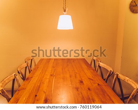 Wooden table and wooden chairs. A lamp hanging above the tabe and a clock on the wall. Toned image.