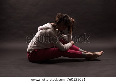 Picture of the emotion of grief. Girl in depression on a dark background. She holds her hair in her hands. The mood of the picture is emotion of sorrow