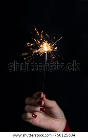Young woman her hand holding Bengal light on black background