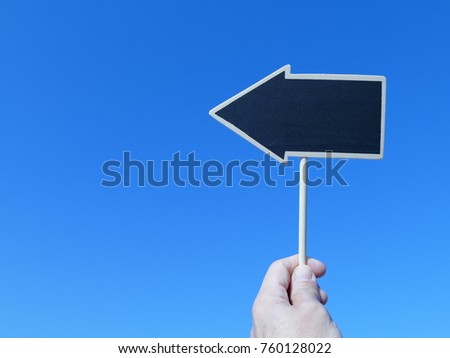 a hand holding arrow shape of chalkboard  with the blue sky background