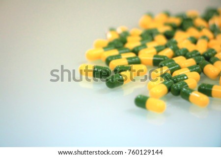 Blurred photo of antibiotics green - yellow capsules on glass background with copy space.