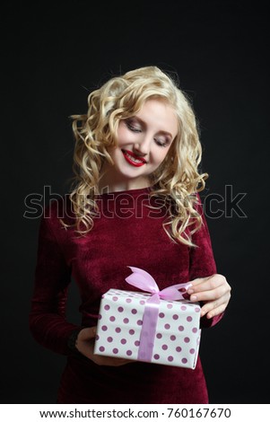Beautiful girl in a burgundy dress with a gift on a black background.