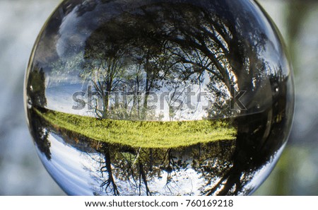 close up view on beautiful landscape trees in blue sky and green meadow through lens ball sphere, france