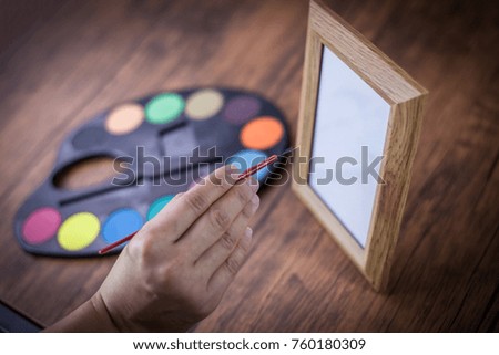 The concept's creation as the field of the image. Handle brushes Set of watercolor paints, and palette for art drawing to picture frame Placed on a wooden table . Customize colors Vintage retro tone