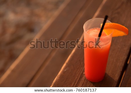 Colorful cocktail in wooden bench at Ibiza during sunset. Orange tequila sunrise over wood stairs in San Antonio, focused glass on one side and blurred background at the other. Soft beautiful light.