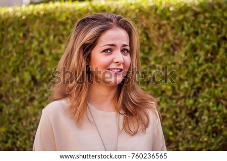 A cute European girl with a shy and confused look standing outside. Worried girl student before the exam session.
 
