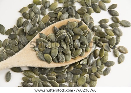 Green tasty organic pumpkin seeds; peeled kernels of pumpkin on wooden spoon on white background. Vegan and vegetarian super foods. Seeds and grains healthy diet.