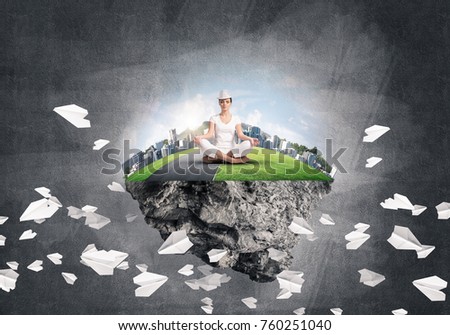 Woman in white clothing keeping eyes closed and looking concentrated while meditating on island in the air among flying paper planes with gray dark wall on background. 3D rendering.