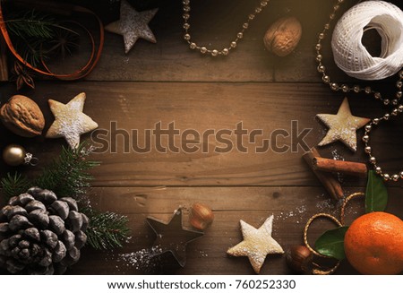 A Christmas background of cookies, sugar powder, nuts, spices, baking molds, fir-tree branch, and pine cones on rustic background.