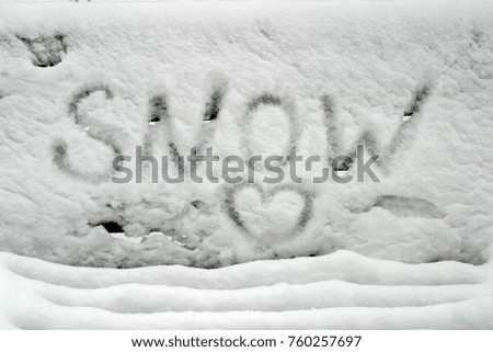 The inscription "Snow" and the symbol of the heart on a bench in a park covered with white and pure snow.
