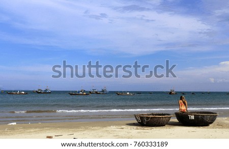 Beautiful girl in bikini sitting on a colorful boat, and watching the fishing ships in the distance