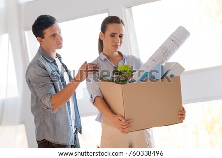 Touch. Calm understanding young man touching the shoulder of his sad dismissed wife standing with a box of personal items