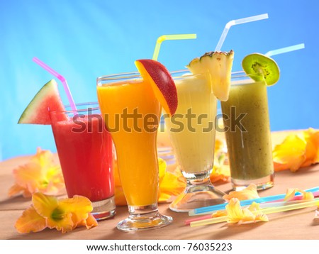 Mango, pineapple, watermelon and kiwi smoothie with drinking straws surrounded by gladiolus flower on wood (Selective Focus, Focus on the mango smoothie in the front) Royalty-Free Stock Photo #76035223