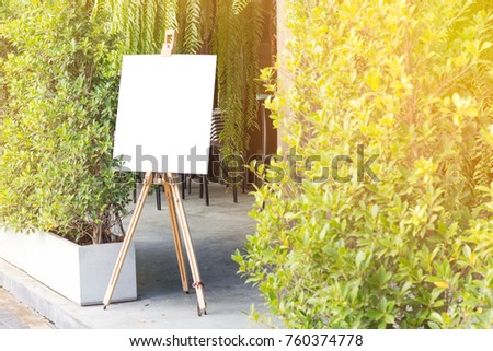 A blank sign with easel is standing beside trees. Green background.