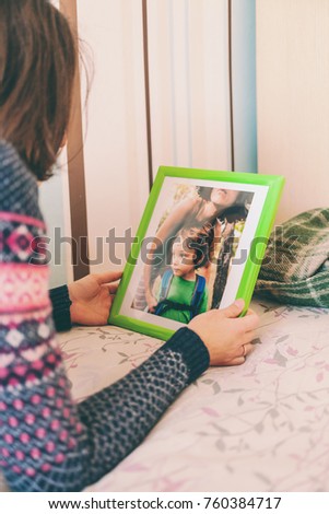 A woman looks at a photo of a boy. Mom holds a photo frame with a photograph of her son. A small child and memories.