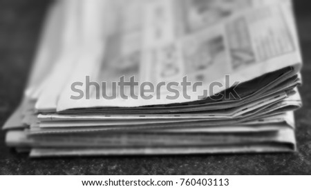 Pile of old newspapers on dark horizontal surface. Background texture, side view, blurred