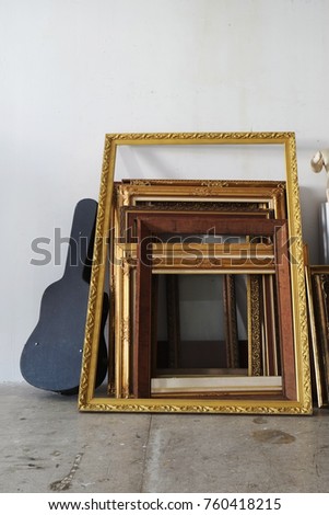 Old vintage golden photograph frames leaning against the wall with guitar case