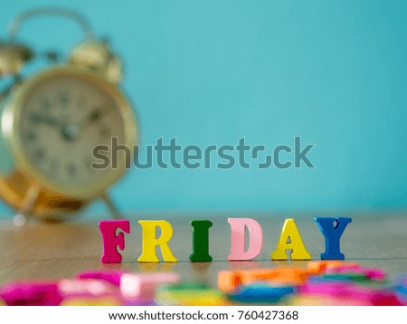 Colorful wooden word FRIDAY on wooden table and vintage alarm clock and background is powder blue. English alphabet made of wooden letter color.