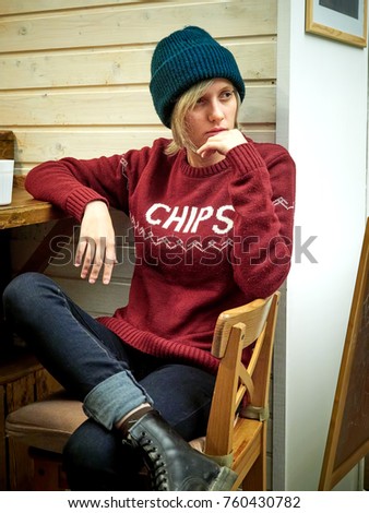 Young hipster woman in hat and sweater sitting in cafe