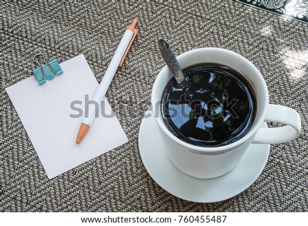 Black coffee and a note pad are placed on the mat.