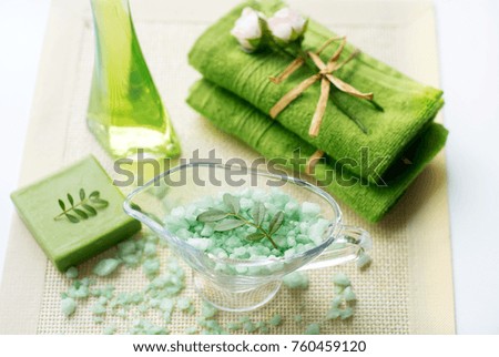 Spa kit: liquid soap, sea salt, green towel, fresh flowers, olive leaves on an old yellow napkin