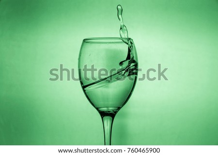 Wineglass with splashing drops of fresh water - motion freeze close-up picture isolated on the green background.