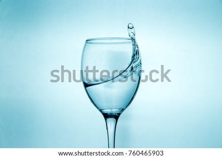 Wineglass with splashing drops of fresh water - motion freeze close-up picture isolated on the blue background.