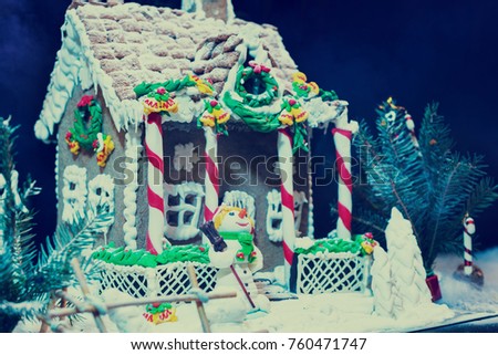 Delicious big gingerbread house, sprig of Christmas tree and a sugar mastic snowman on dark background. Mockup for seasonal offers and holiday post card