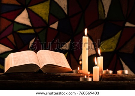 Bible and candle on a old oak wooden table.  Beautiful Stained-glass windows background.Religion concept.