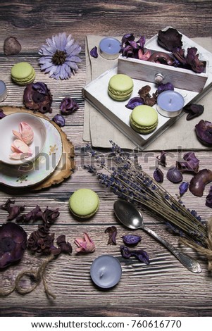 Beautiful table picture: macaroons, silver plate, tea couple (cup and small plate), dry flowers, candles, book, cotton cloth at wooden background