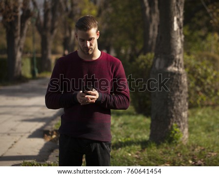 Young Fashion man in red T-shirt posing in park and looking at telephone