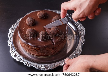 A man's hand with a kitchen knife above a chocolate homemade biscuit cake on a metal plate Royalty-Free Stock Photo #760643287