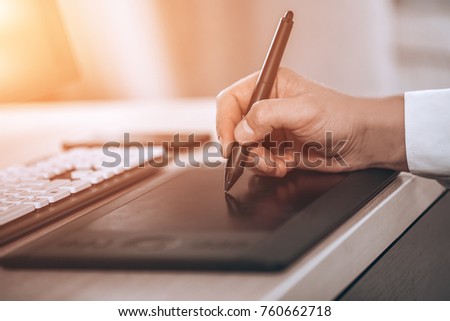 Graphic designer's workspace. Hand on pen tablet. Young smart man in the office. Free black monitor copy space for design. Warm glare of sun light.