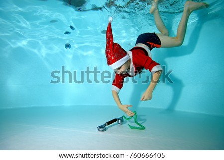 A little boy in a cap and suit of Santa Claus dives to the bottom of the pool to retrieve a toy. Portrait. Taking pictures underwater in the pool. Horizontal orientation