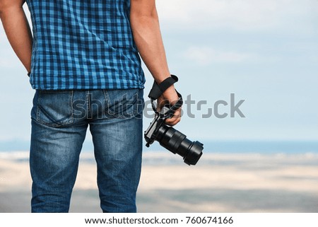 View of the man's back standing in front of the sea and holding a digital camera in his hands, copy space.