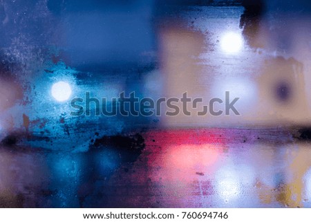 abstract blurred texture of night city behind wet misted glass of window. atmospheric cold blue bokeh background.