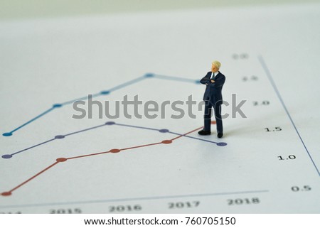 Miniature businessman standing and thinking on printed analysis chart or graph as business yearly review or leadership concept.