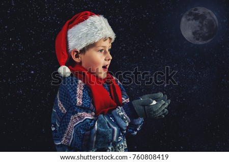 Happy boy in Santa hat plays with snowflakes on a dark background . Happy Christmas holidays