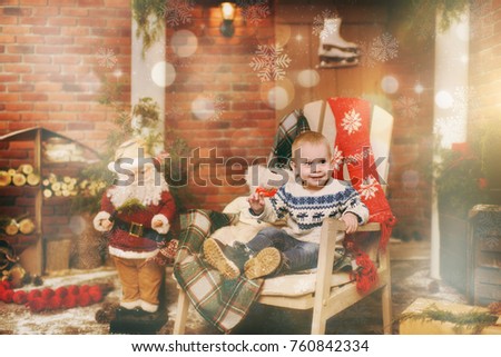 Happy little child boy dressed in sweater sitting on the chair with Santa in decorated New Year room at home. Christmas good mood. Family and holiday 2018 concept. Magical highlight bokeh effect.