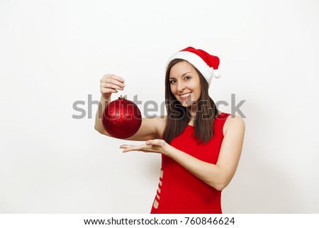 The beautiful European brunette young happy woman with charming smile in red dress and Christmas hat holding big shiny tree toy on white background. Santa girl isolated. New Year holiday 2018 concept